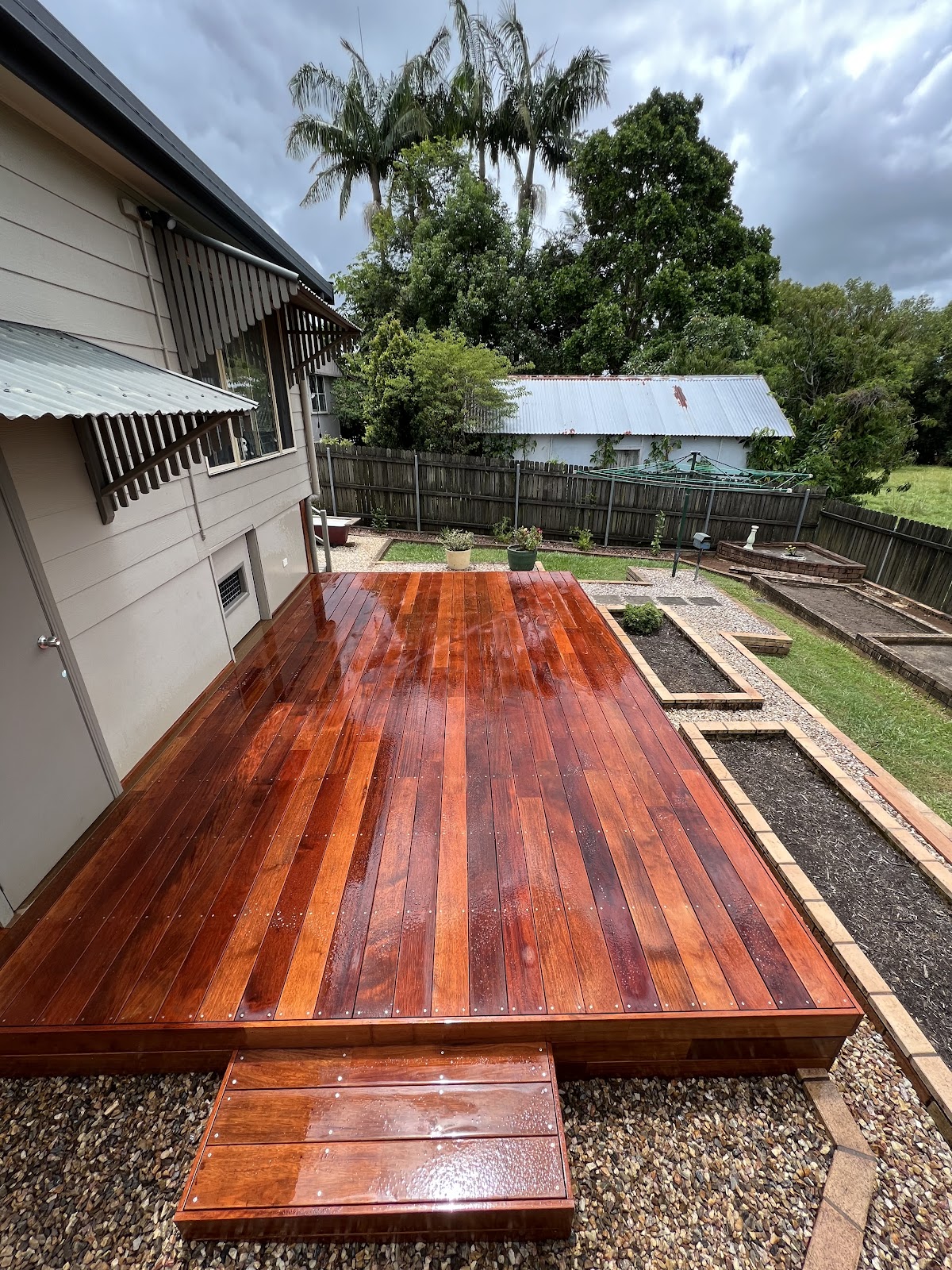 Freshly oiled red timber deck with a step, beside a weatherboard house